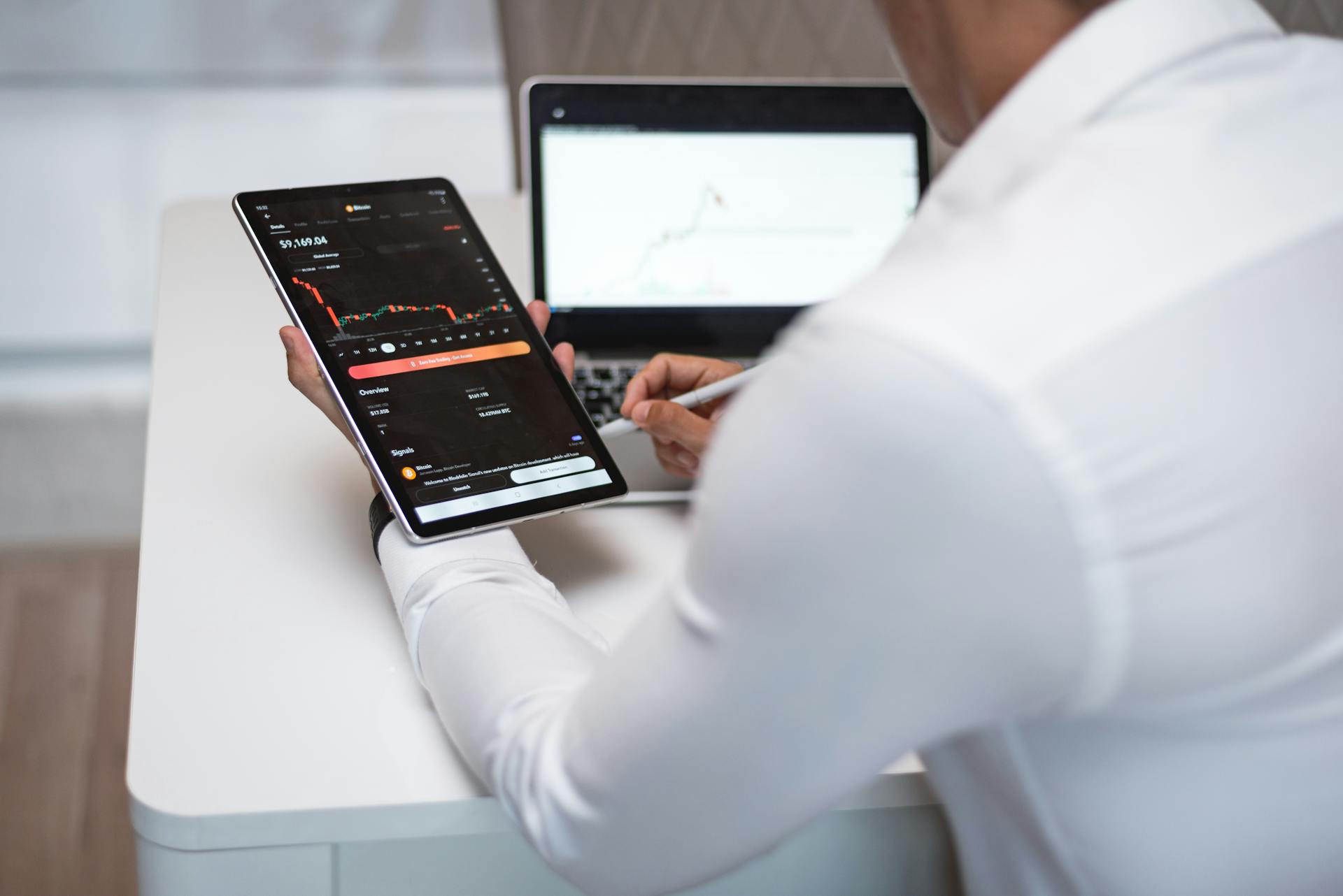 Businessman analyzing financial charts on tablet and laptop in modern office.