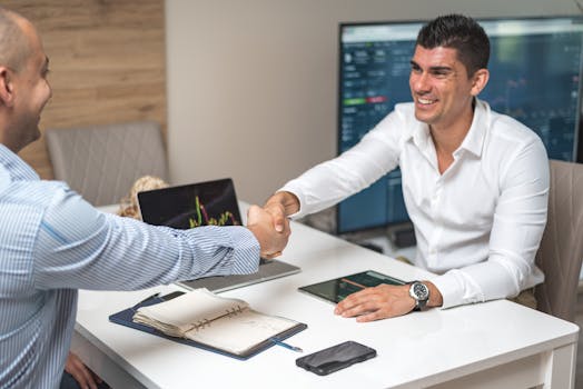 Two businessmen shaking hands in a modern office, indicating a successful deal or agreement.
