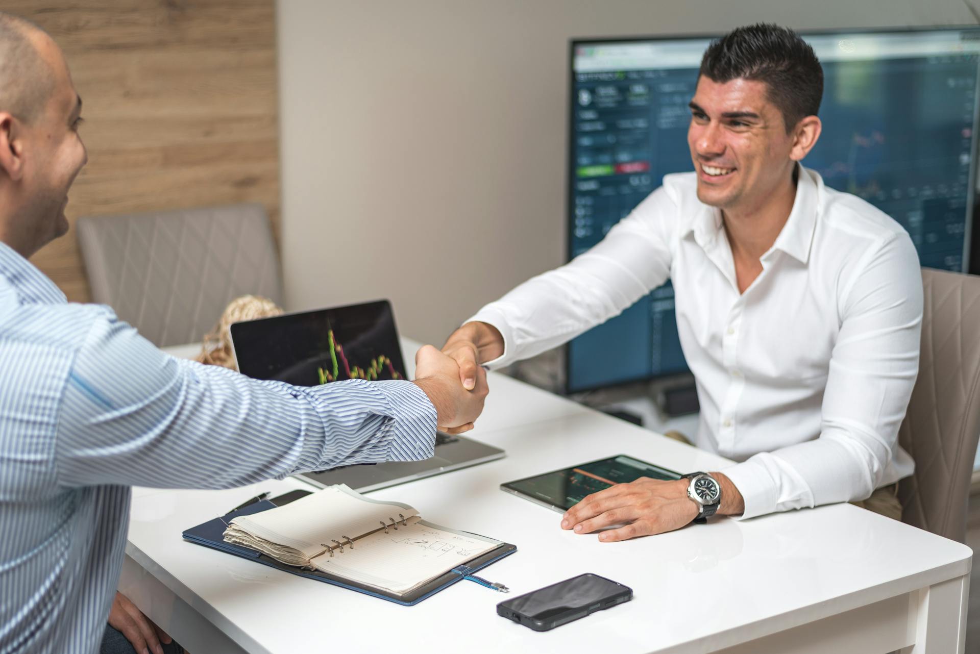 Two businessmen shaking hands in a modern office, indicating a successful deal or agreement.