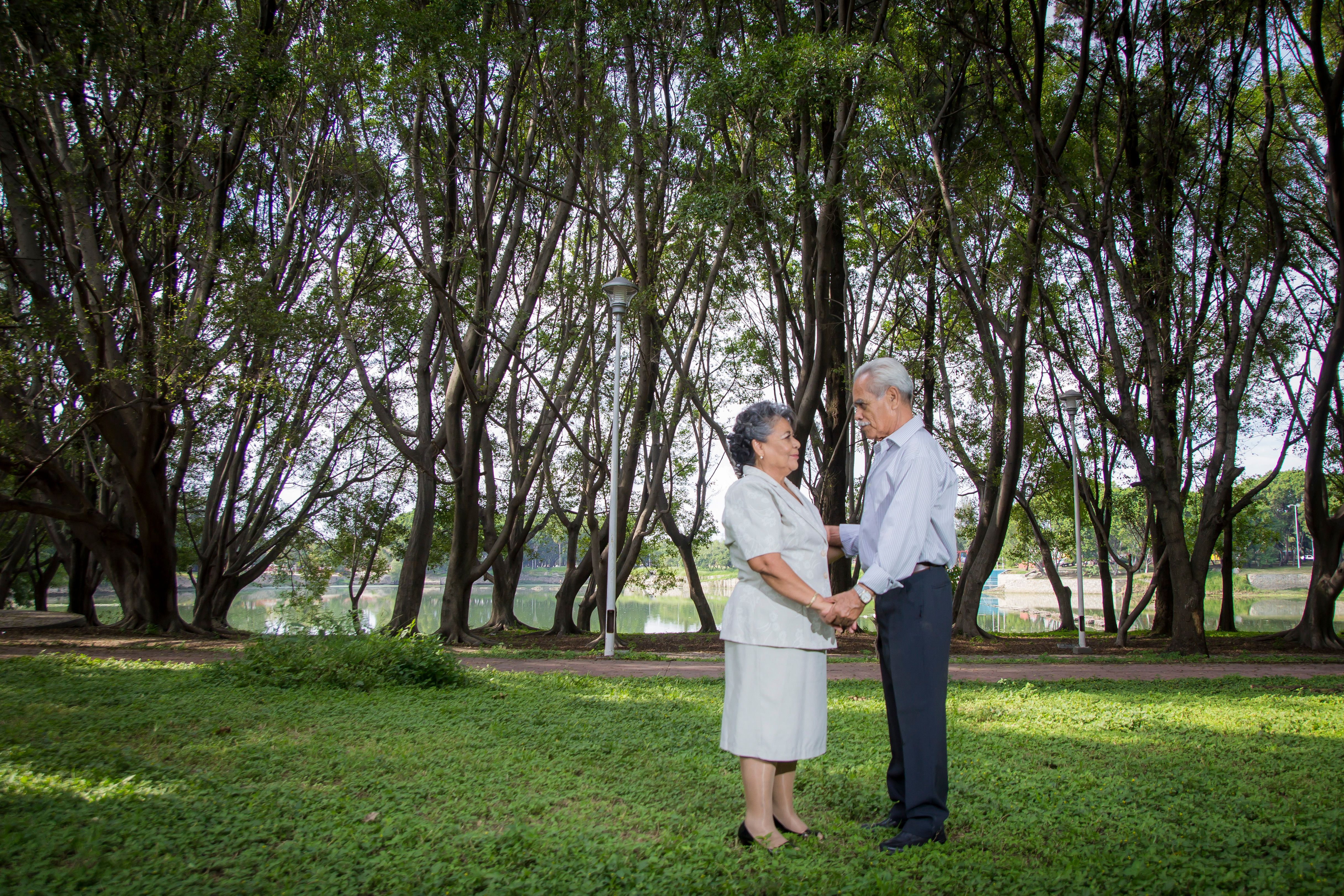 A senior couple standing and holding hands in a lush green park setting.