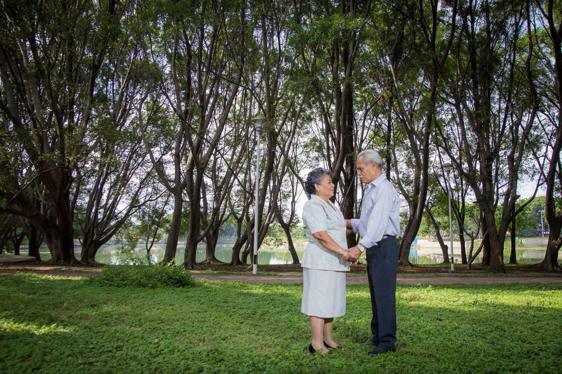 A senior couple standing and holding hands in a lush green park setting.