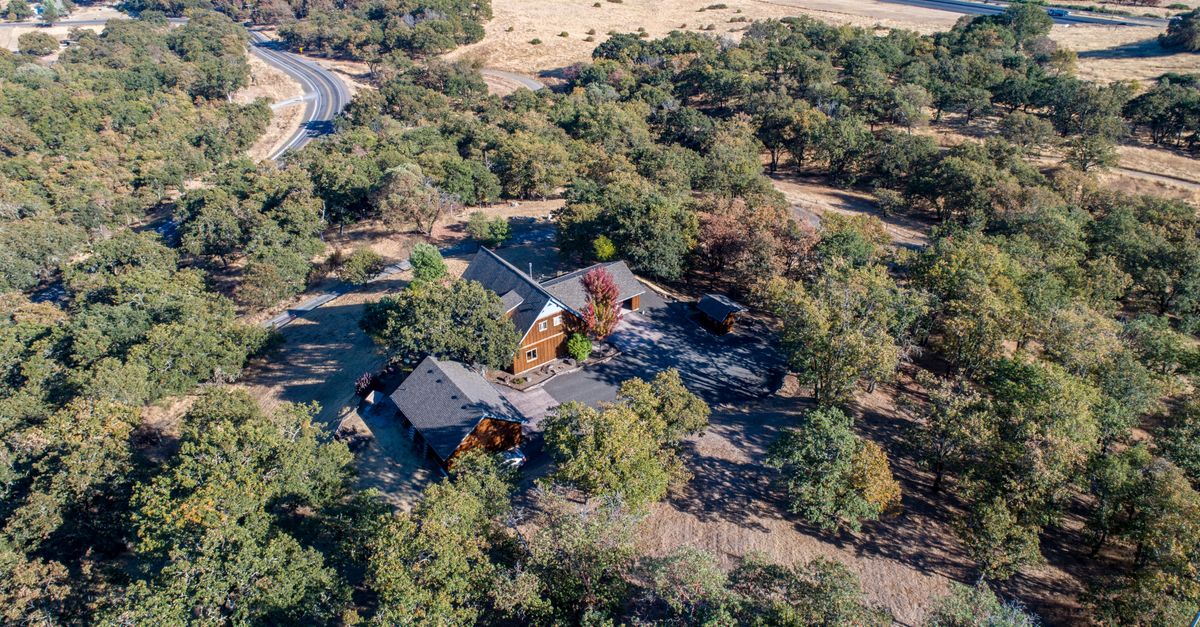 Aerial view showcasing a house surrounded by lush green trees in a scenic landscape.