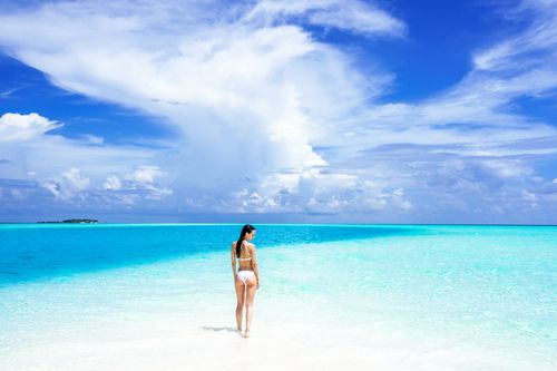 Free A woman in a bikini stands on a pristine beach with turquoise water under a vibrant summer sky. Stock Photo