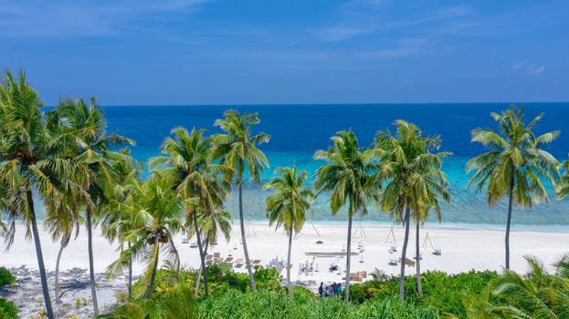 Stunning aerial view of a tropical beach with white sands and lush palm trees against a vibrant turquoise sea.