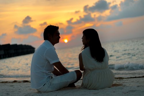 Free A couple sitting on a sandy beach, enjoying a beautiful sunset over the ocean. Stock Photo
