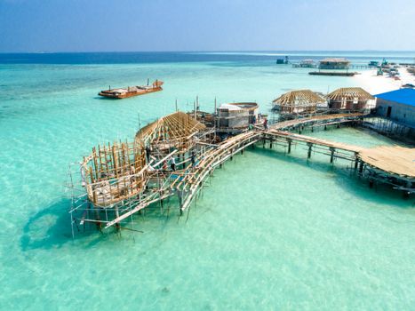 Aerial view of wooden bungalows being constructed over turquoise waters in the Maldives.