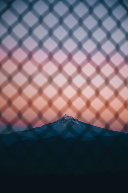 Picturesque landscape through metal grid of mountain located in highlands under cloudless sky in sundown