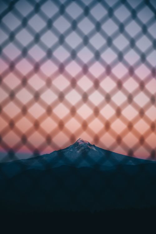 Free Picturesque landscape through metal grid of mountain located in highlands under cloudless sky in sundown Stock Photo