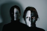 Unemotional models with face painted in white and black paints standing in room with light wall and looking at camera