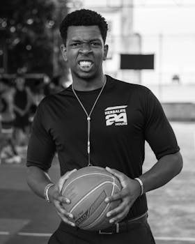 Black and white photo of an African American male basketball player holding a ball with an intense expression.