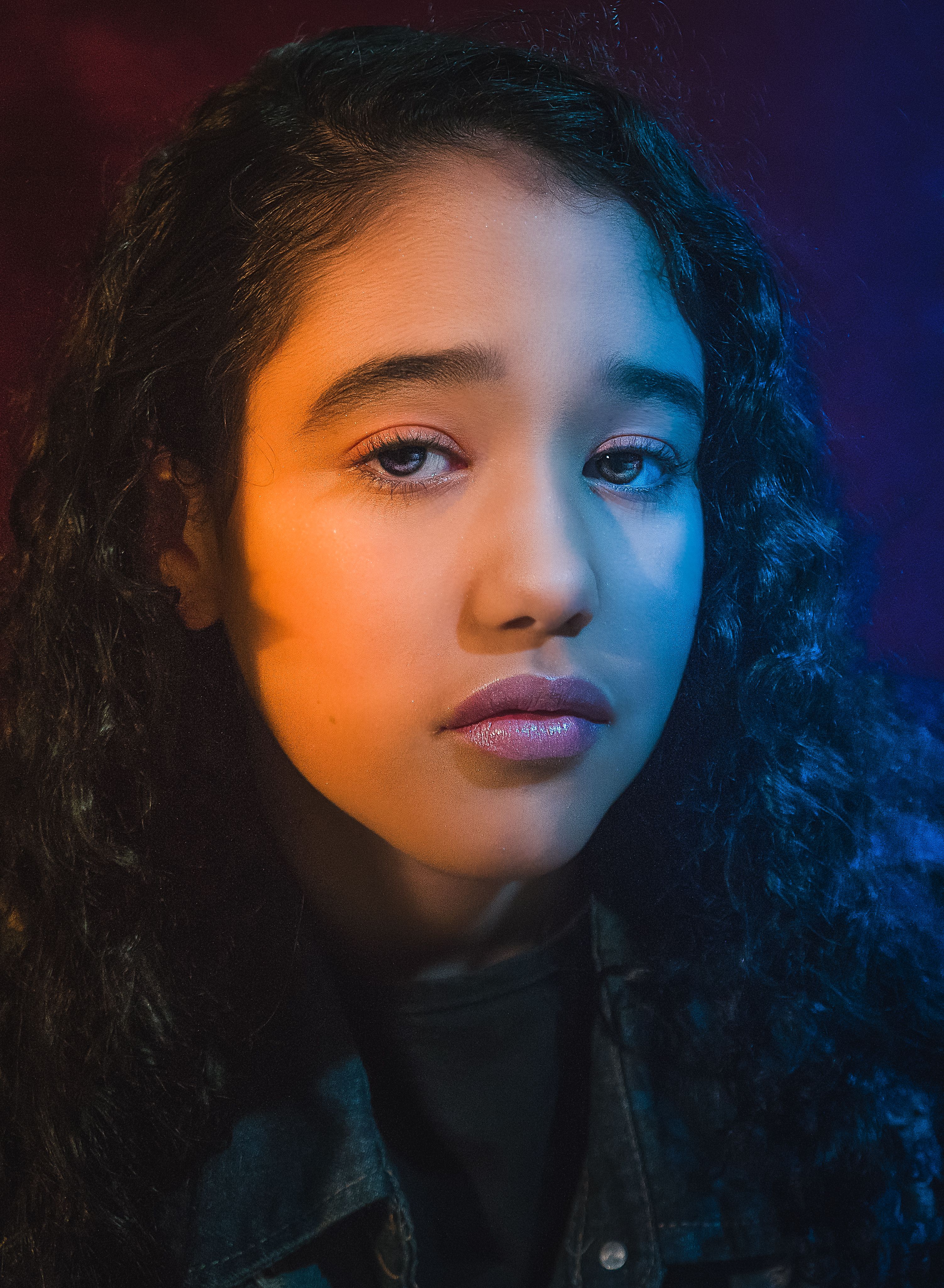 A dramatic portrait of a young woman with curly hair in colorful lighting.