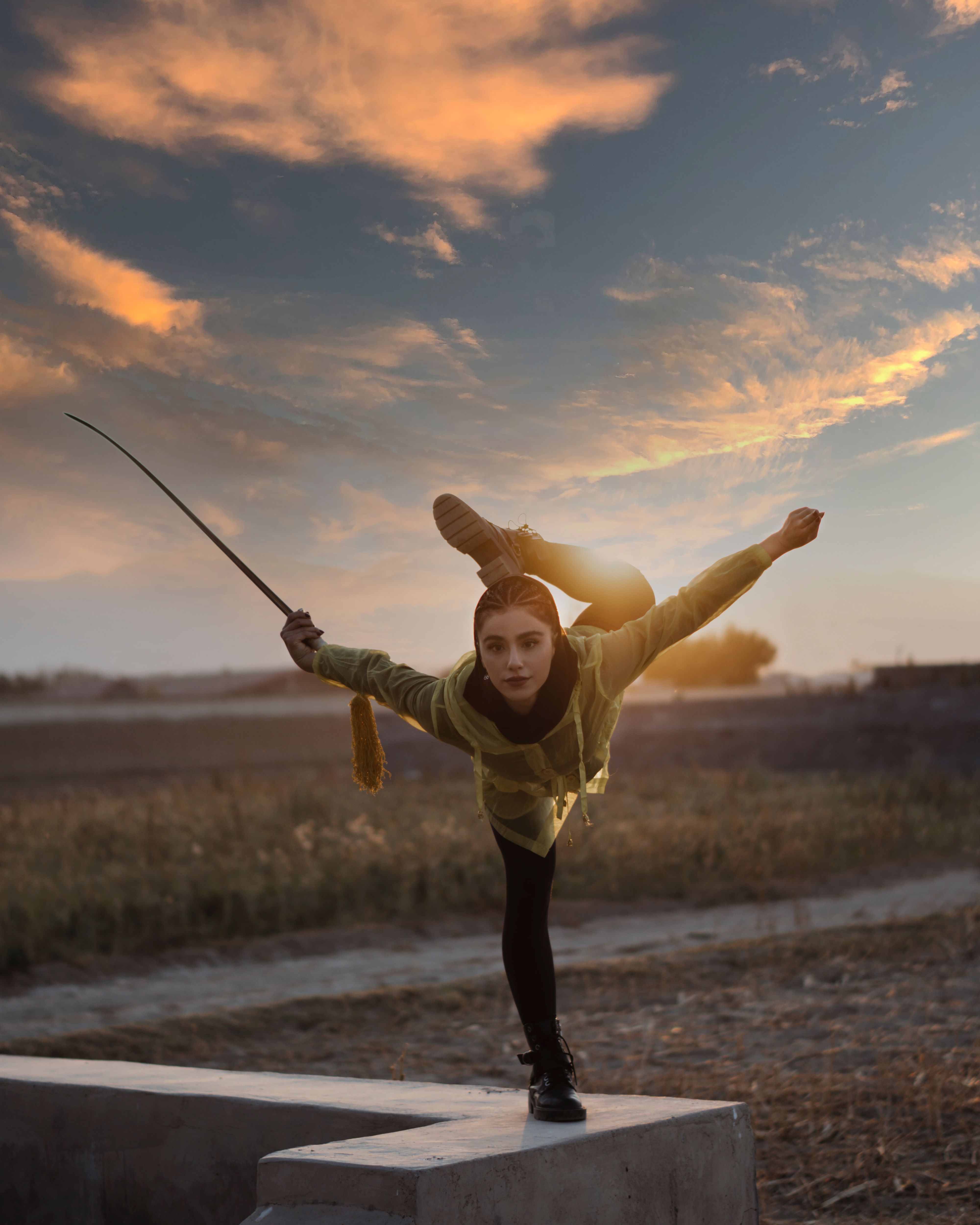 A young woman performs an athletic martial arts pose on a block at sunset.