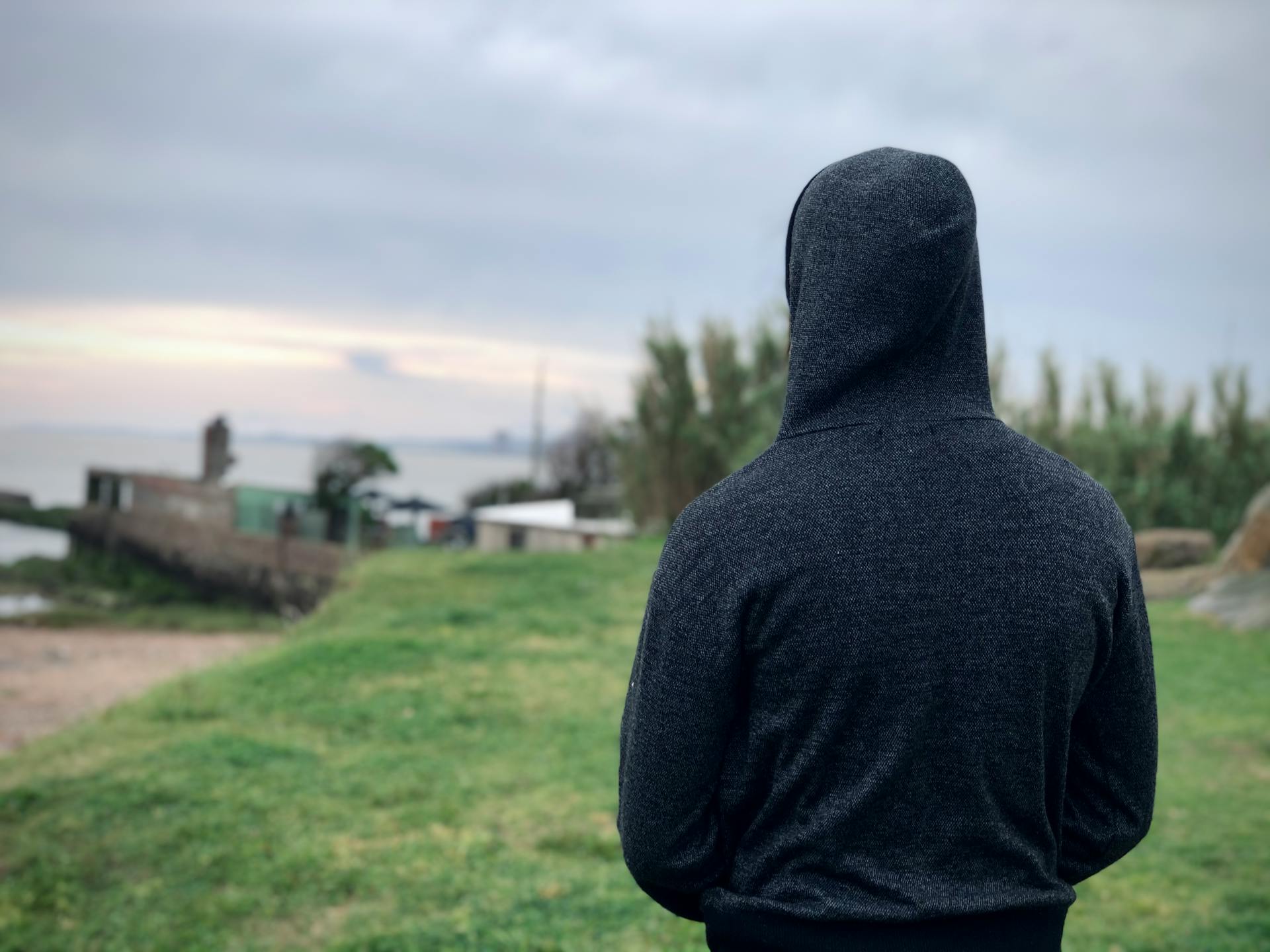 A person in a gray hoodie stands outdoors, gazing at the Montevideo coastline.