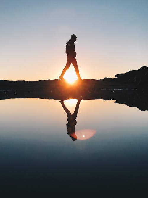 Silhouet Van De Mens Die Op Rotsformatie In De Buurt Van Waterlichaam Tijdens Zonsondergang