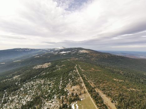 Stunning aerial shot of Krkonoše Mountains with snow patches and lush forests.