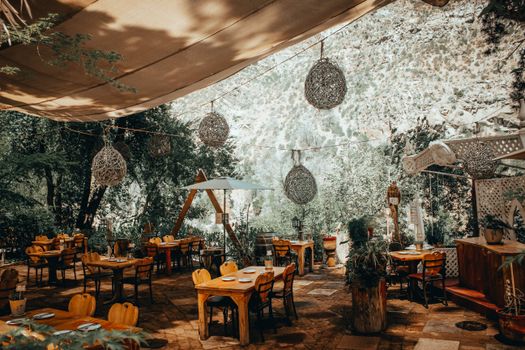 Cozy outdoor dining area with wooden tables and chairs under a canopy, surrounded by nature.