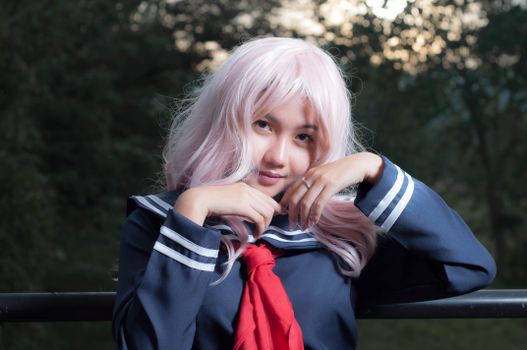 Beautiful Asian woman posing outdoors in a sailor outfit with pink hair.