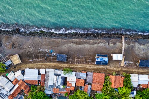 Free Aerial view of houses with green trees on coast against wavy ocean in summer Stock Photo