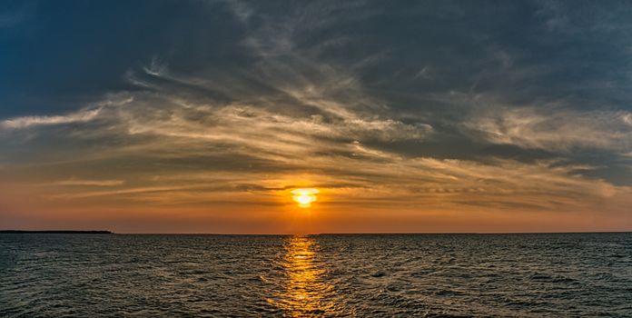 Scenery view of endless rippled ocean with horizon under glowing sun in bright sky at sundown