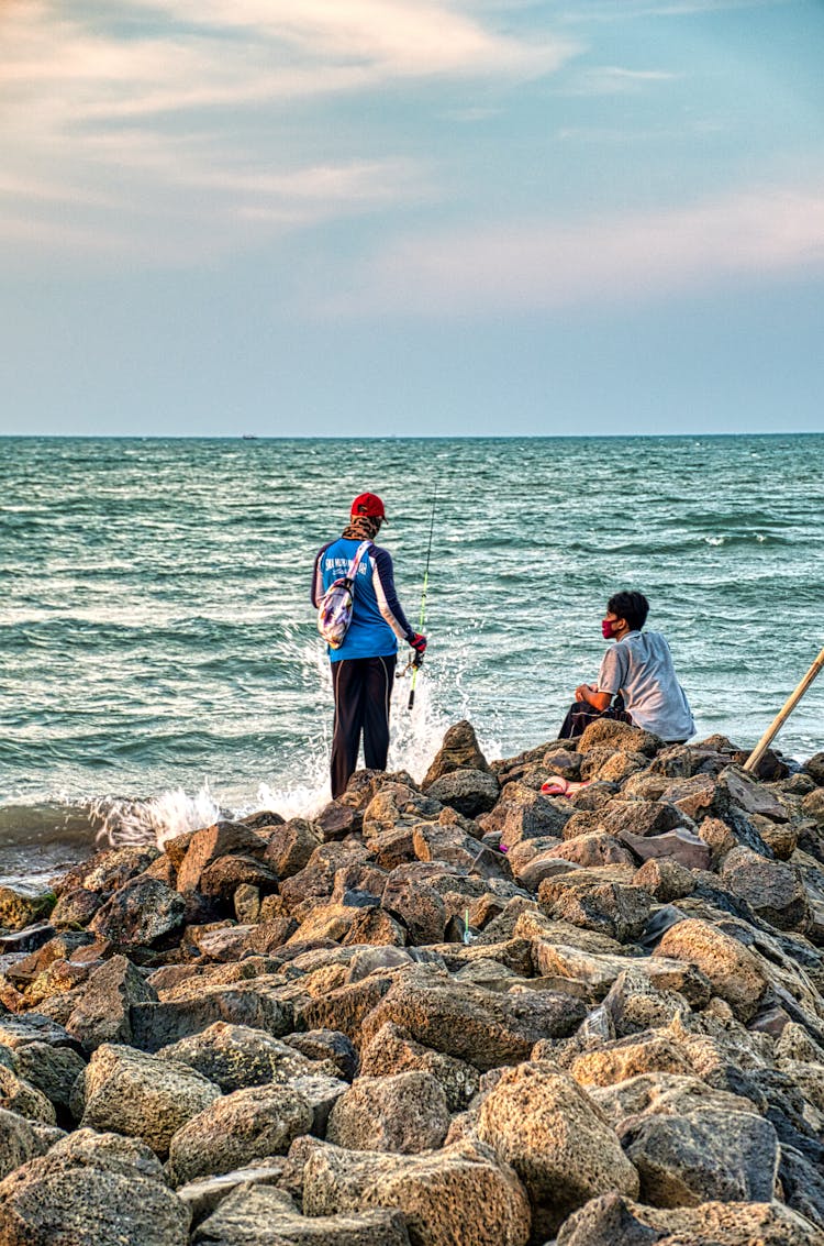 Unrecognizable Fishermen Catching Fish In Ocean From Stone Coast