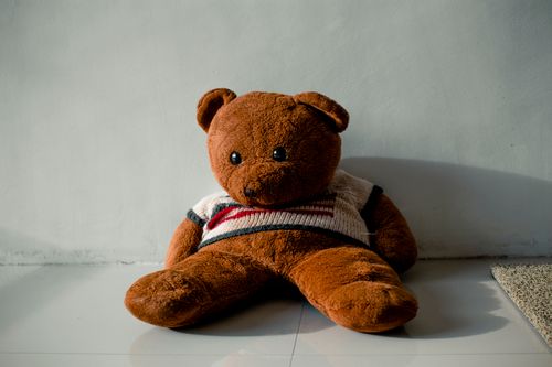 Free Soft bear in knitwear on ceramic floor against carpet on sunny day on light background Stock Photo