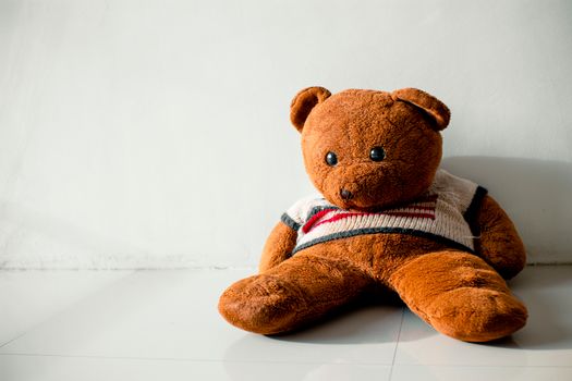 Plush bear in sweater with striped ornament on tiled floor with shades on sunny day on white background