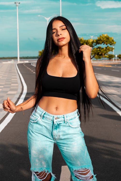 Woman in Black Tank Top and Blue Denim Jeans Standing on the Road