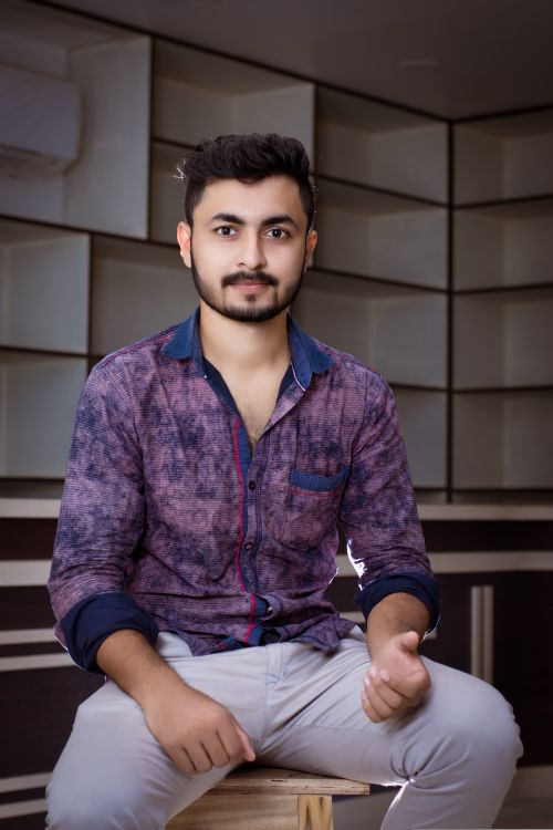 Free Portrait of a young man with a beard sitting on a stool indoors, exuding a casual and confident look. Stock Photo