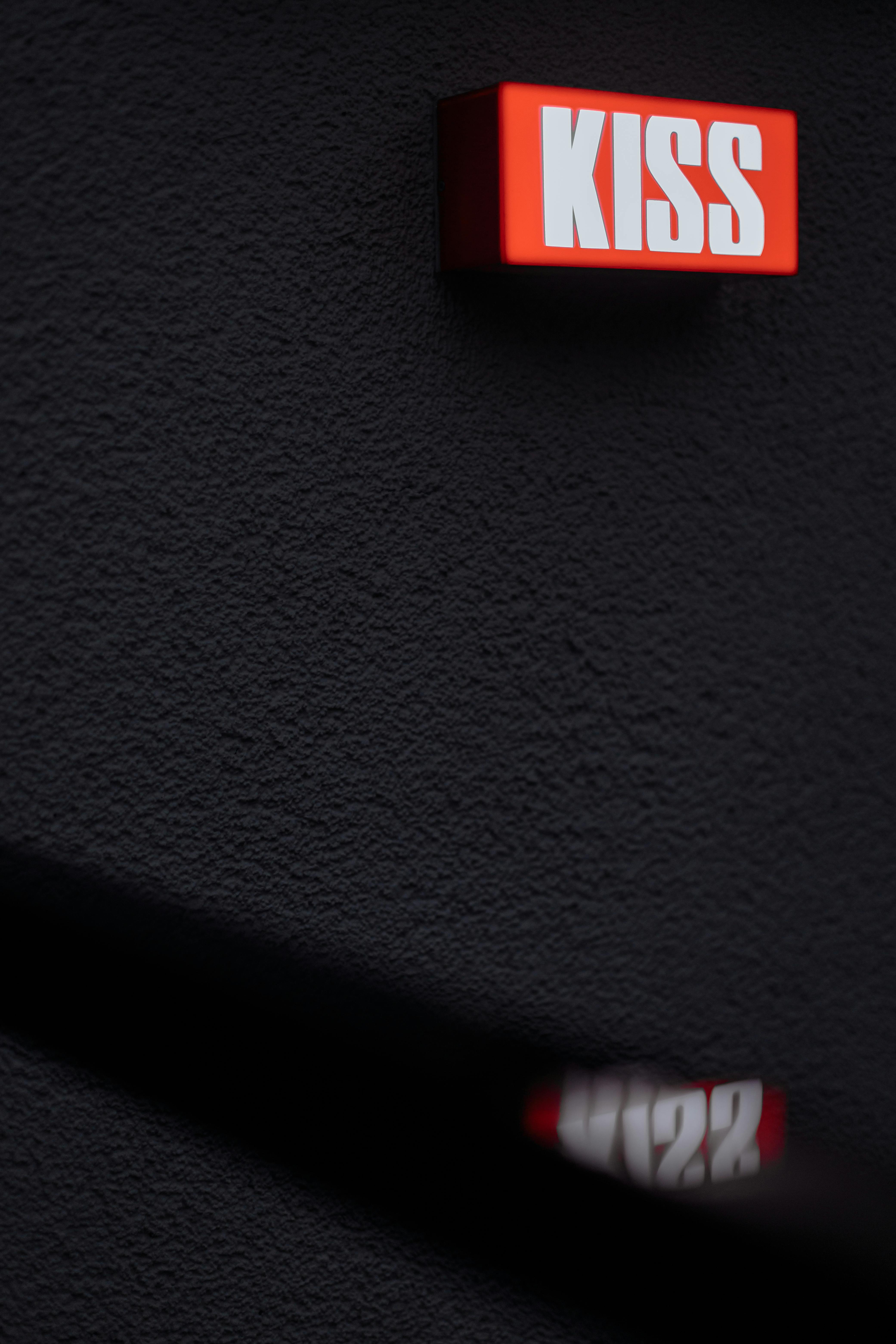 Vivid red 'KISS' sign on a black wall creates a striking visual contrast.