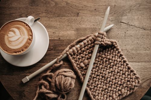 Free A warm cappuccino with latte art beside knitting needles and yarn on a rustic table. Stock Photo