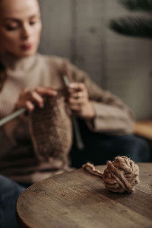 Free A woman focuses on knitting while a yarn roll lies on a wooden table indoors. Stock Photo