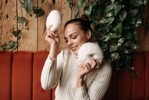 Free A joyful woman dressed in a turtleneck sweater, holding balls of yarn indoors. Stock Photo