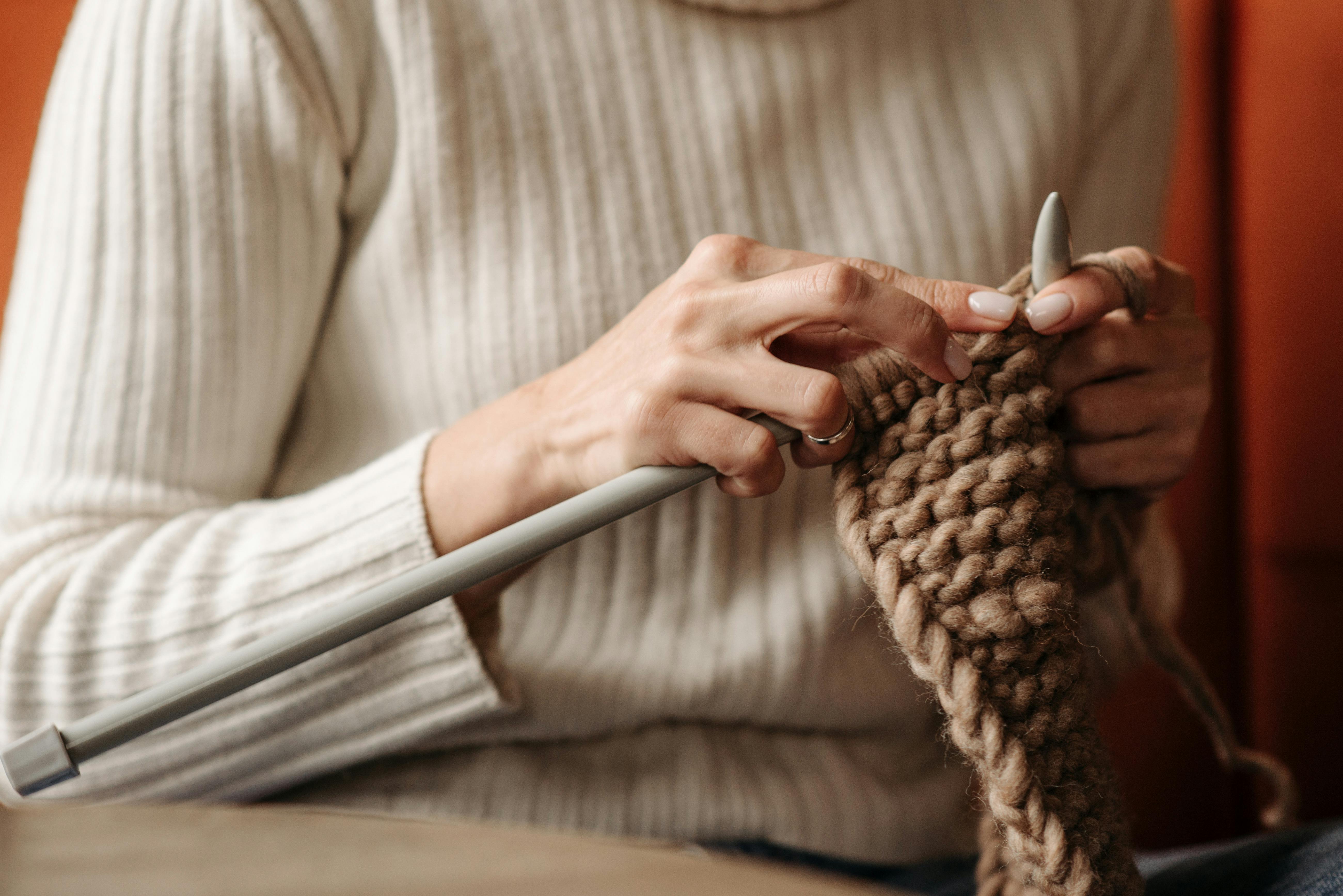 Close-up of a woman knitting with thick yarn and needles indoors.