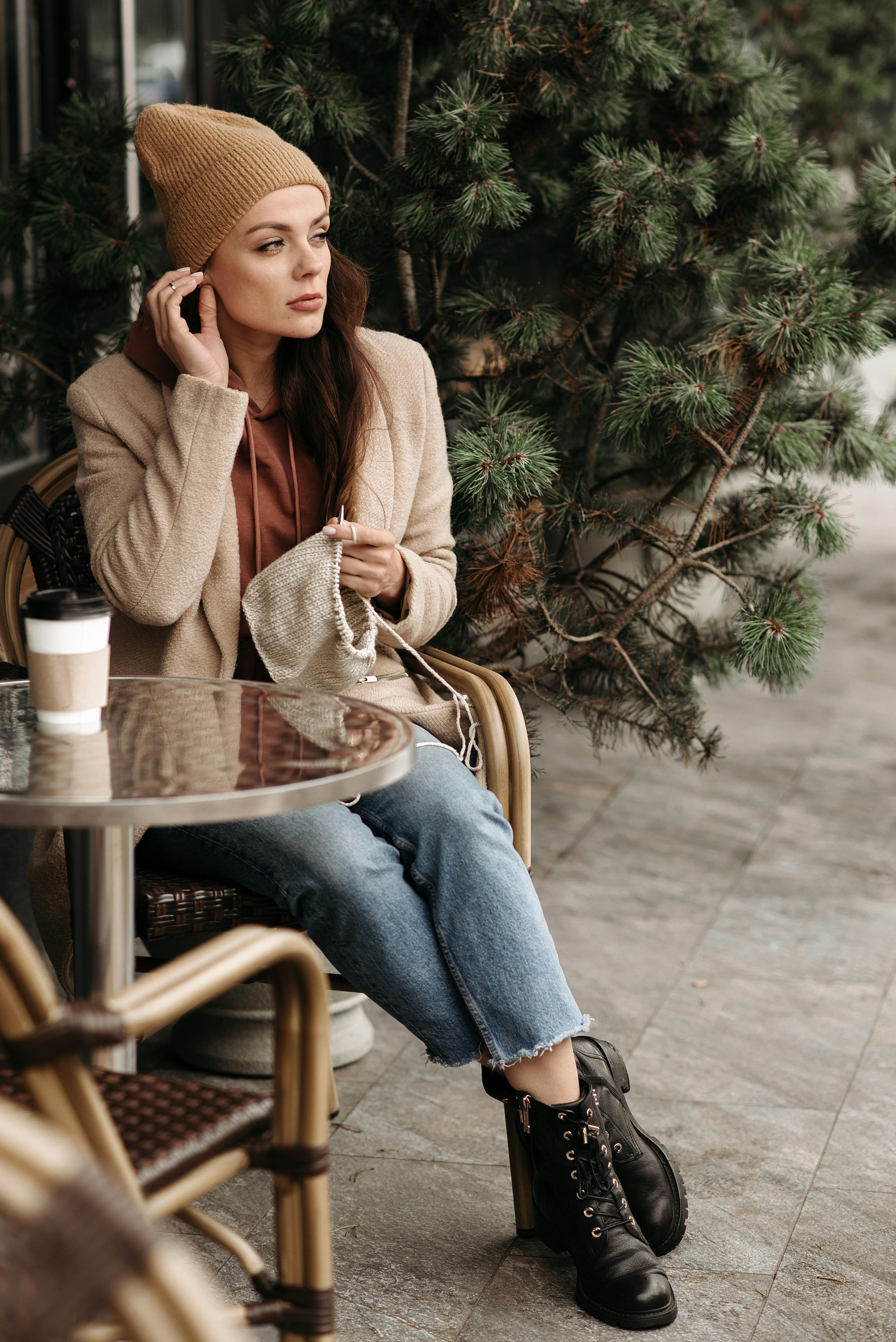 A woman enjoys knitting outdoors on a fall day with a coffee beside her.