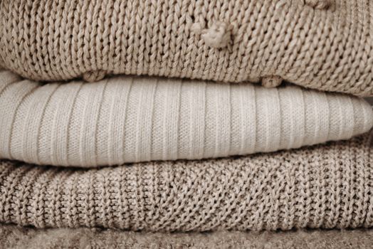 Textured close-up of stacked beige knit sweaters showcasing various knitting patterns.