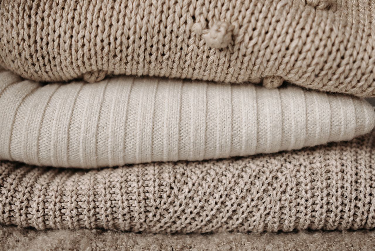 textured close up of stacked beige knit sweaters showcasing various kn