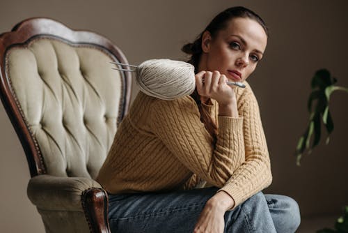 Woman in Brown Sweater and Blue Denim Jeans Sitting on an Arm Chair