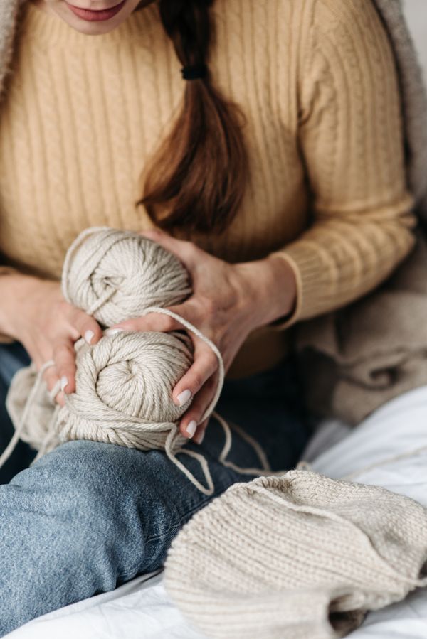 Person knitting with beige yarn in a warm room — photo by Pavel Danilyuk on Pexels