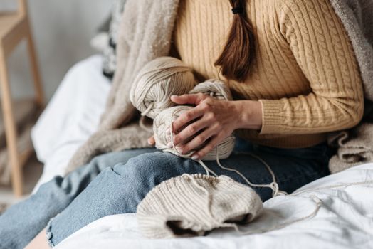 Female knitter crafting with beige yarn on a cozy bed, embodying a warm indoor setting.