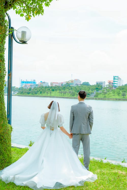 Free Man and Woman Standing on Green Grass Near Body of Water Stock Photo