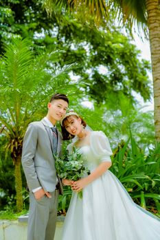 Lovely couple in wedding attire posing amidst lush greenery.