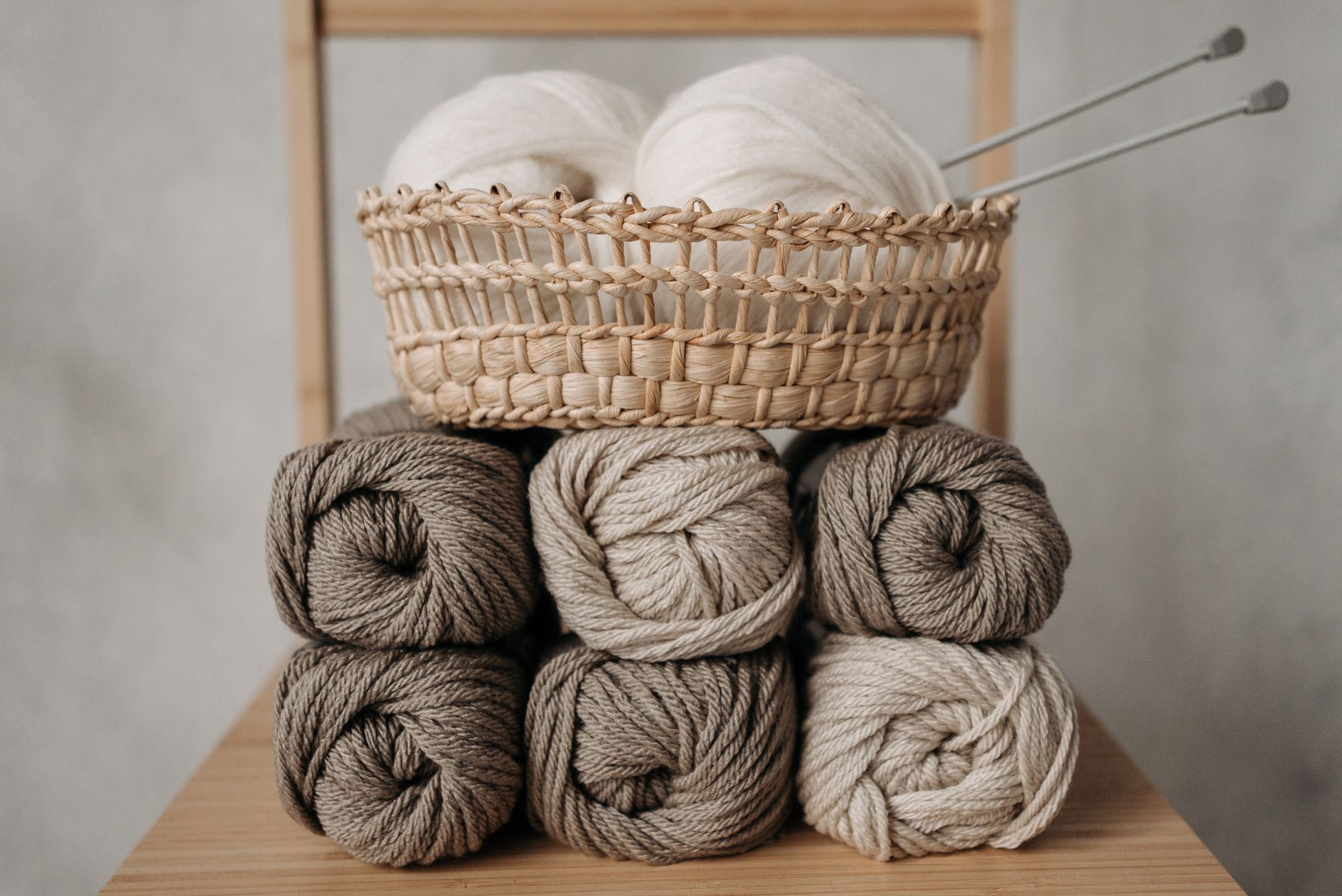 Stacked yarn balls in a wicker basket with knitting needles, ideal for crafting projects.