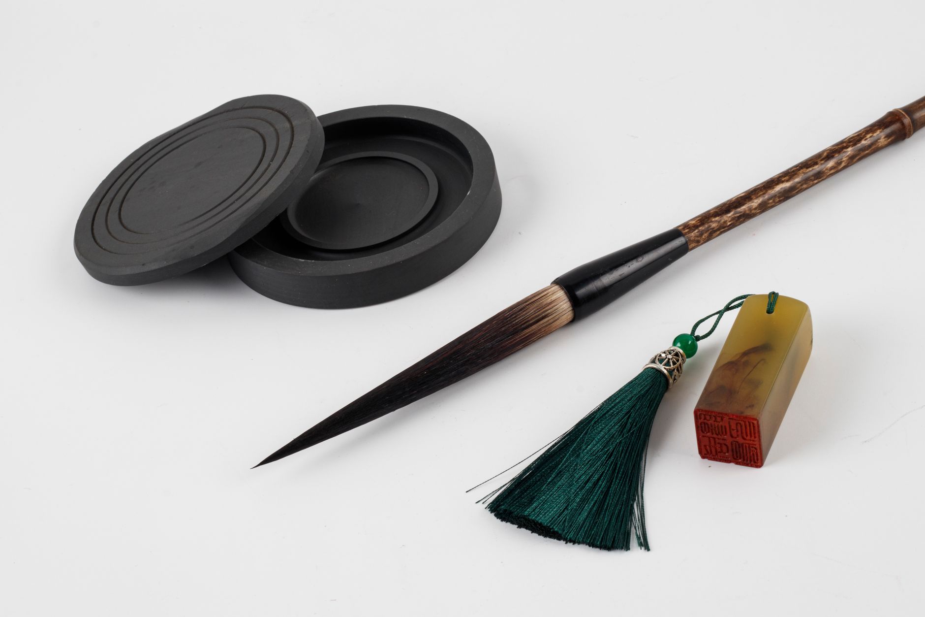 Close-up of traditional Asian calligraphy tools including ink stone, brush, and seal on white background.