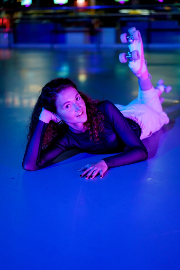 A smiling skater lying on the neon-lit rink floor in quad skates