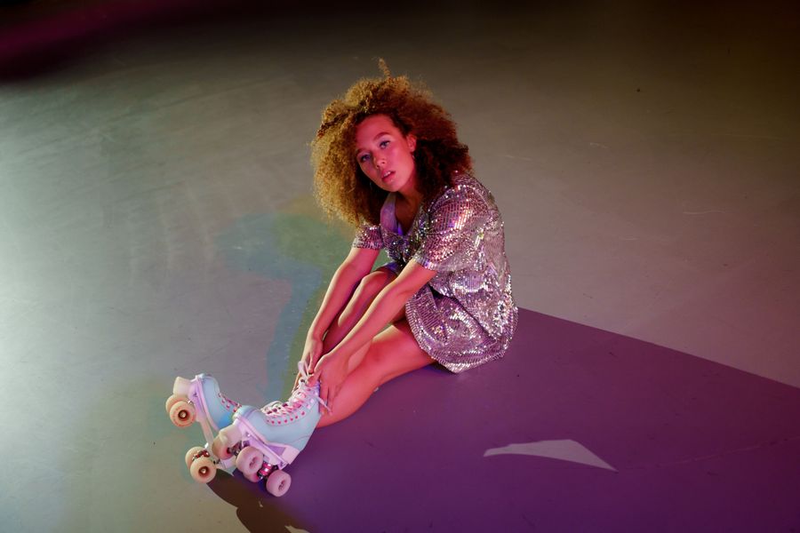 A skater in a sparkling sequin outfit sitting on the rink floor with retro roller skates