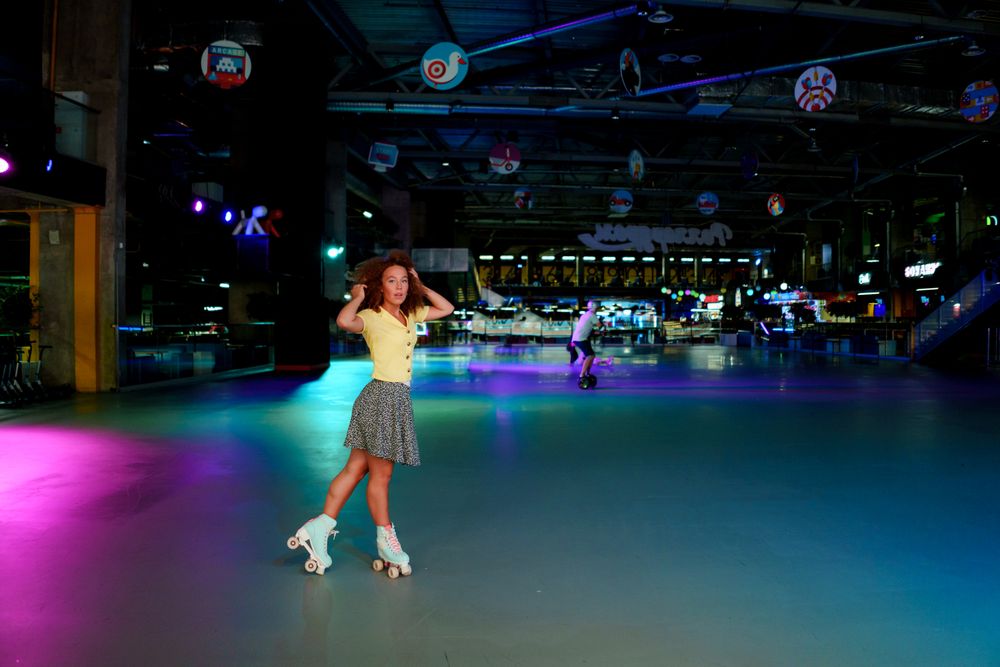 A skater in a yellow top rolling through a neon-lit indoor rink