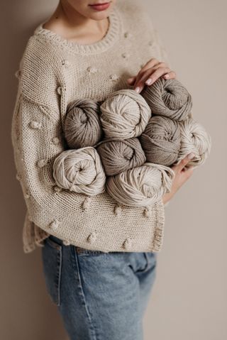 Armful of undyed wool skeins held against a knitted jumper — Pavel Danilyuk on Pexels