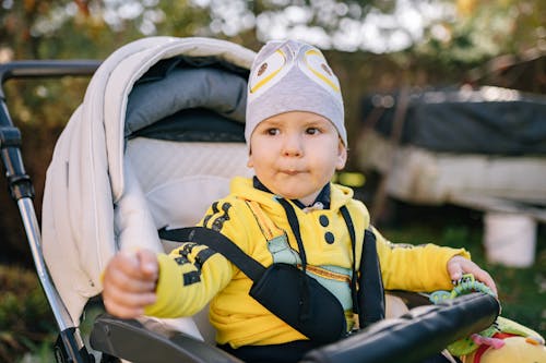 A Cute Baby in Yellow Jacket Sitting on a Baby Stroller