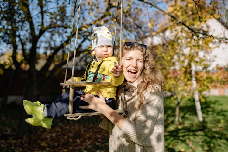 Woman Standing Behind A Toddler On A Swing