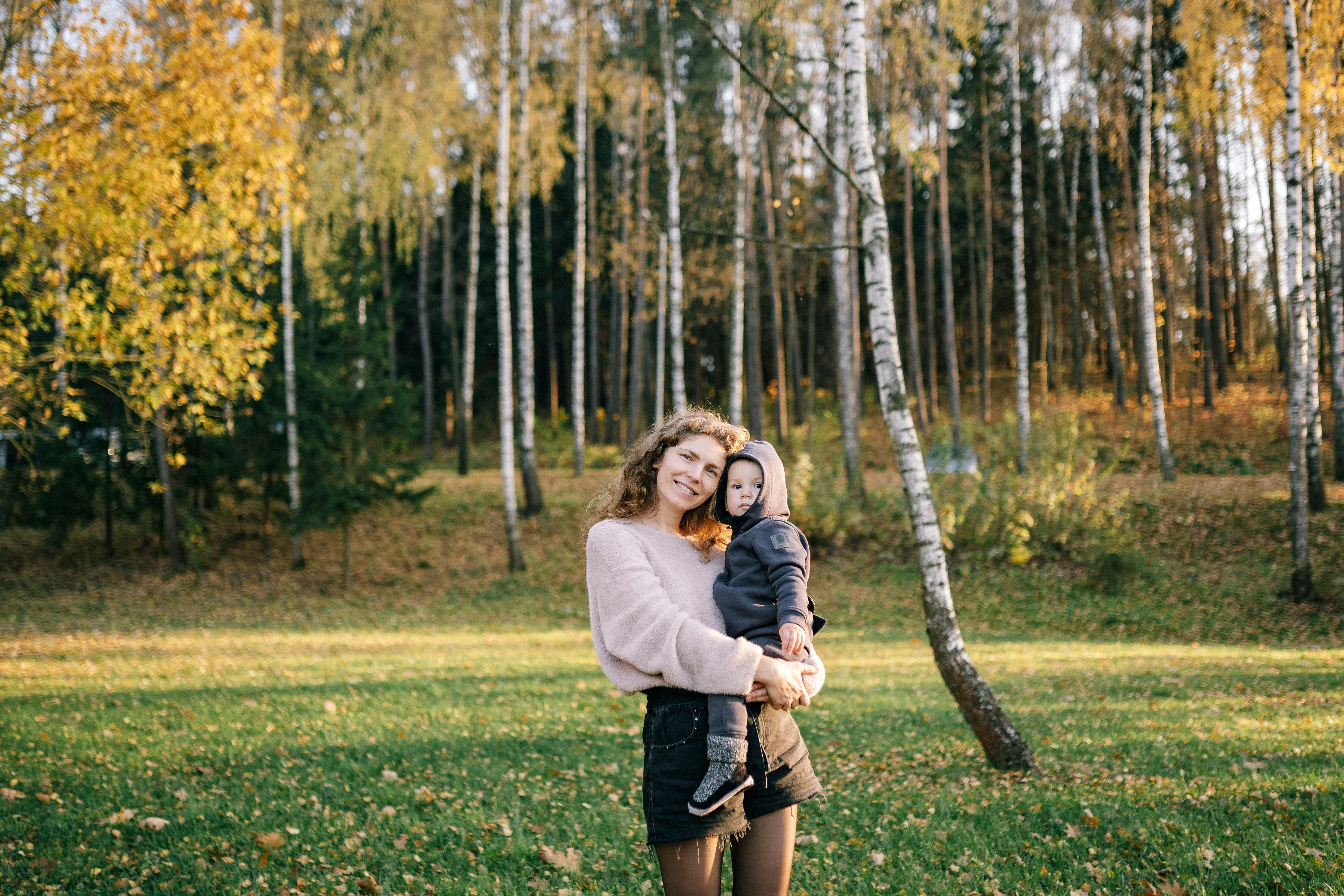 A joyful mother holding her child outdoors in an autumn forest setting.